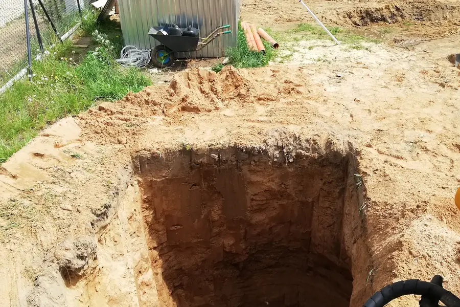Wykop pod przyłącze kanalizacyjne, obok rury kanalizacyjne i blaszany garaż